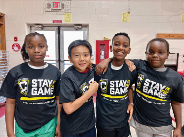 boys standing in a row smiling wearing stay in the game shirts